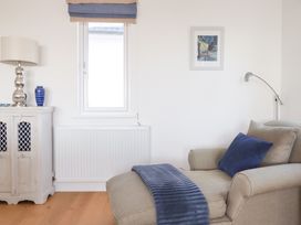 A living room with a beige armchair with blue cushions a blue throw a white cabinet with a lamp and vase and a window at The Old Harbour Masters House in Fowey