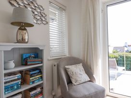 A corner with a grey armchair and a cushion near a bookshelf and a glass door at The Old Harbour Masters House in Fowey