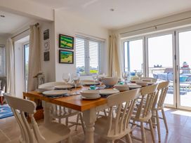A dining room with a wooden table set with plates bowls and glasses surrounded by white chairs and windows at The Old Harbour Masters House in Fowey