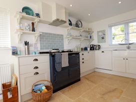 A kitchen with white cabinets open shelves and a blue stove with basket on the floor at The Old Harbour Masters House in Fowey