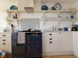 A kitchen with white cabinets a dark stove towels hanging open shelves with dishes and a wall clock at The Old Harbour Masters House in Fowey