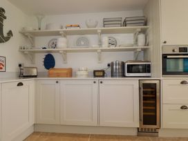 A kitchen with white cabinets shelves holding plates bowls and baskets a toaster bread box microwave oven and wine cooler at The Old Harbour Masters House in Fowey