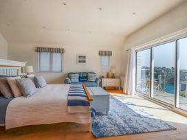 A bedroom with a bed a sofa a chest of drawers and large windows overlooking a balcony at The Old Harbour Masters House in Fowey