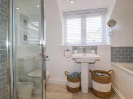 A bathroom with a shower, toilet, pedestal sink, two baskets with towels, and a window with blinds at The Old Harbour Masters House in Fowey