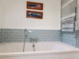 A bathroom with a white bathtub blue tiled walls a chrome faucet and a towel on a heated towel rail at The Old Harbour Masters House in Fowey