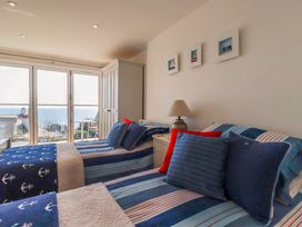 A bedroom with two beds blue bedding a lamp and balcony doors with sea view at The Old Harbour Masters House in Fowey