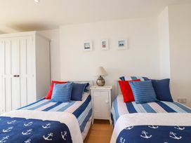 A bedroom with two single beds with blue striped bedding and anchor blankets a white nightstand with a lamp and a white wardrobe at The Old Harbour Masters House in Fowey