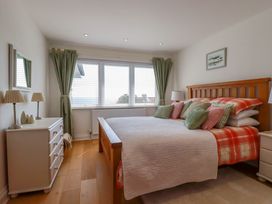 A bedroom with a wooden bed with cushions and a white dresser with lamps by a window at The Old Harbour Masters House in Fowey