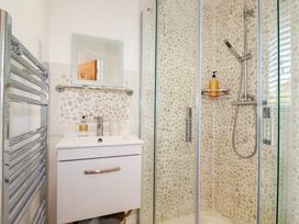 A bathroom with a shower enclosure with pebble pattern tiles a sink with a mirror and a chrome towel radiator at The Old Harbour Masters House in Fowey