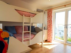 A bedroom with white bunk beds red and blue cushions side table with lamp and glass doors with red curtains at The Old Harbour Masters House in Fowey