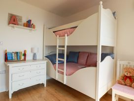 A children's bedroom with a white bunk bed a white chest of drawers with books and a lamp and a chair with a teddy bear at The Old Harbour Masters House in Fowey