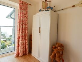 A room with a white wardrobe a wooden child's high chair with a teddy bear and red patterned curtains next to a glass door at The Old Harbour Masters House in Fowey