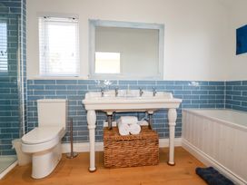 A bathroom with a toilet double sink bathtub blue tiled walls and wooden floor at The Old Harbour Masters House in Fowey