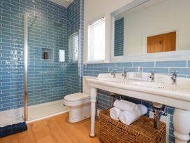 A bathroom with a shower, toilet, double sink, mirror, and wicker basket at The Old Harbour Masters House in Fowey
