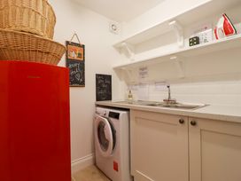 A laundry room with a red refrigerator washing machine a sink countertop shelves and wicker baskets at The Old Harbour Masters House in Fowey