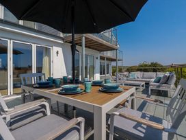 An outdoor patio with a dining table set with blue dishes and cups under a large umbrella and a seating area with sofas and cushions at The Old Harbour Masters House in Fowey