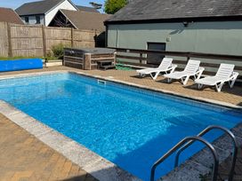An outdoor swimming pool with a metal handrail surrounded by tiled floor and three white lounge chairs next to a wooden fence and a hot tub at Tig Bhan in Llanteg