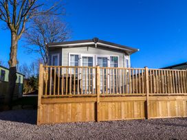 A wooden deck with railing in front of a small gray house with glass doors and windows at 2 Willow Way near Lytham