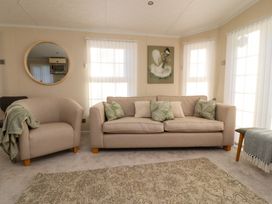A living room with beige sofa and armchair green and white cushions a round wall mirror and a wall painting at 2 Willow Way near Lytham
