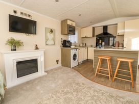 A kitchen area with a washing machine dining stools and a wall-mounted tv above a fireplace at 2 Willow Way near Lytham