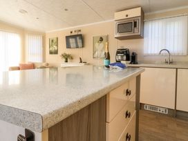 A kitchen with a countertop and sink next to a living area with a sofa and wall TV at 2 Willow Way near Lytham