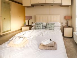 A bedroom with a bed pillows nightstands lamps and folded towels with slippers on the bed at 2 Willow Way near Lytham