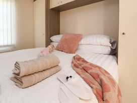 A bedroom with a bed with white sheets with folded towels a throw and slippers on the bed at 2 Willow Way near Lytham