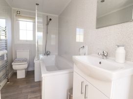 A bathroom with a bathtub shower unit a toilet a sink with a cabinet and a window at 2 Willow Way near Lytham