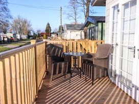 A wooden deck with two wicker chairs and a round glass table outside a building at 2 Willow Way near Lytham