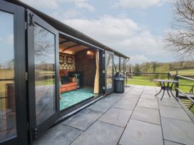 An outdoor patio with stone tiles and a small round table next to a glass door leading to a room with a leather sofa and green carpet at GWR Wagon - Victoria Station in Ludlow