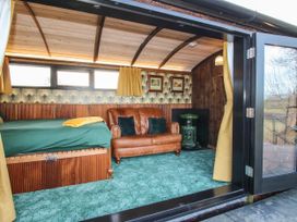 An interior room with a brown leather sofa a green carpet a bed with green bedding and yellow curtains at GWR Wagon - Victoria Station Ludlow