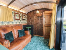 A living area with a brown leather sofa with green cushions a green side table wooden walls and yellow curtains at GWR Wagon - Victoria Station in Ludlow