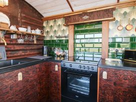 A kitchen with dark brown cabinets a black oven green tiled backsplash and open wooden shelves at GWR Wagon - Victoria Station in Ludlow