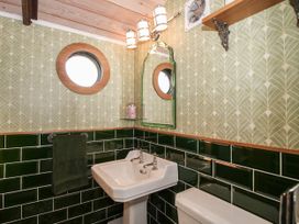 A bathroom with a white sink toilet green tiled walls round window and an arched mirror at GWR Wagon - Victoria Station in Ludlow