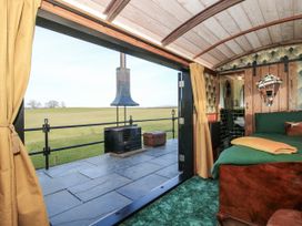 An open room with a bed green carpet and yellow curtains opening to an outdoor patio with a black stove and grassy fields at GWR Wagon - Victoria Station in Ludlow