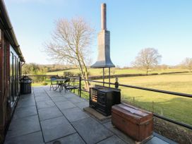 An outdoor patio with black metal railings a stove chimney a wooden chest and a table with chairs overlooking fields at GWR Wagon - Victoria Station in Ludlow