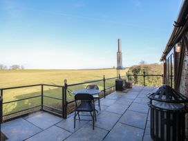 An outdoor patio with a round table two chairs a metal stove and a railing overlooking a grassy field at GWR Wagon - Victoria Station in Ludlow