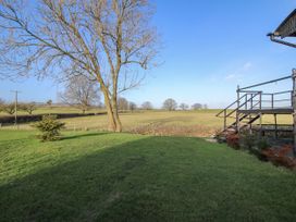 A grassy backyard with a bare tree and metal stairs overlooking open fields at GWR Wagon - Victoria Station in Ludlow