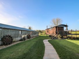 A paved walkway through grass leading to a wooden railway carriage beside a long shed with old wheels against it at GWR Wagon - Victoria Station in Ludlow