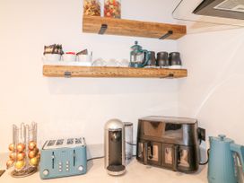 A kitchen counter with a toaster coffee machine air fryer and kettle with jars and cups on wooden shelves at Orchard Retreat Staycation in Kirton
