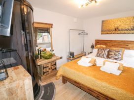 A bedroom with a wooden bed with orange bedding and pillows a wooden vanity with a green bowl sink a round black shower cabin and a window at Orchard Retreat Staycation in Kirton