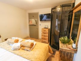 A bedroom with a bed covered with towels a wooden dresser a wall-mounted TV a shower enclosure and a wooden vanity with a sink at Orchard Retreat Staycation in Kirton