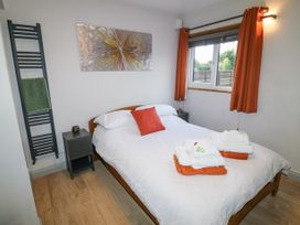 A bedroom with a double bed with orange and white linens bedside tables and a window with orange curtains at Orchard Retreat Staycation in Kirton