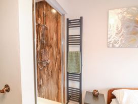 A bathroom shower with a brown marble wall panel next to a black towel radiator with a green towel and part of a bedroom with a bedside table and an artwork on the wall at Orchard Retreat Staycation in Kirton