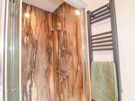 A shower area with a wall-mounted shower head and controls next to a towel radiator with a green towel at Orchard Retreat Staycation in Kirton