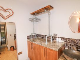 A bathroom with a brown marble countertop wooden cabinets a wall-mounted pipe shelf with hangers a round mirror and a heart-shaped copper wall decoration at Orchard Retreat Staycation in Kirton
