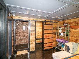 A wooden room with a shower area on the left a sliding wooden door in the center a metal shelf with plants and yoga mats and a cushioned seating area at Orchard Retreat Staycation in Kirton