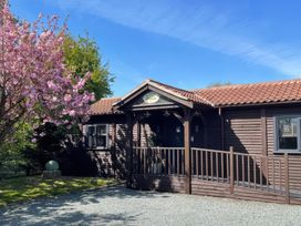 A wooden house with a covered entrance and tiled roof next to a pink flowering tree at Orchard Retreat Staycation in Kirton