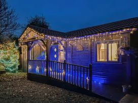 A wooden cabin with string lights on the porch and a decorated tree outside at Orchard Retreat Staycation in Kirton