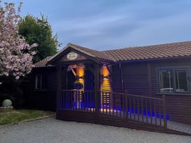 A wooden cabin entrance with a ramp and illuminated lights near a flowering tree at Orchard Retreat Staycation Kirton